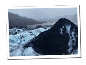 A large black rock is flanked by a pale blue glacier