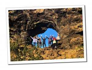 8 people standing within A perfect circle cut naturally through a craggy rock at Dimmuborgir in iceland on a sunny cloudless day