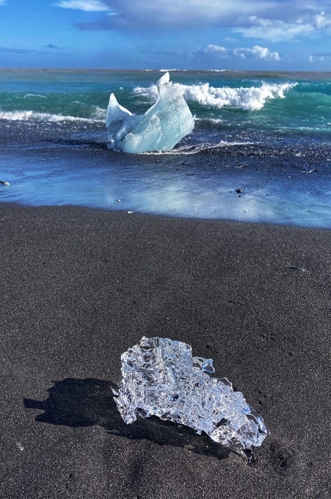 A large ice crystal laying by the shore on a black sand beach