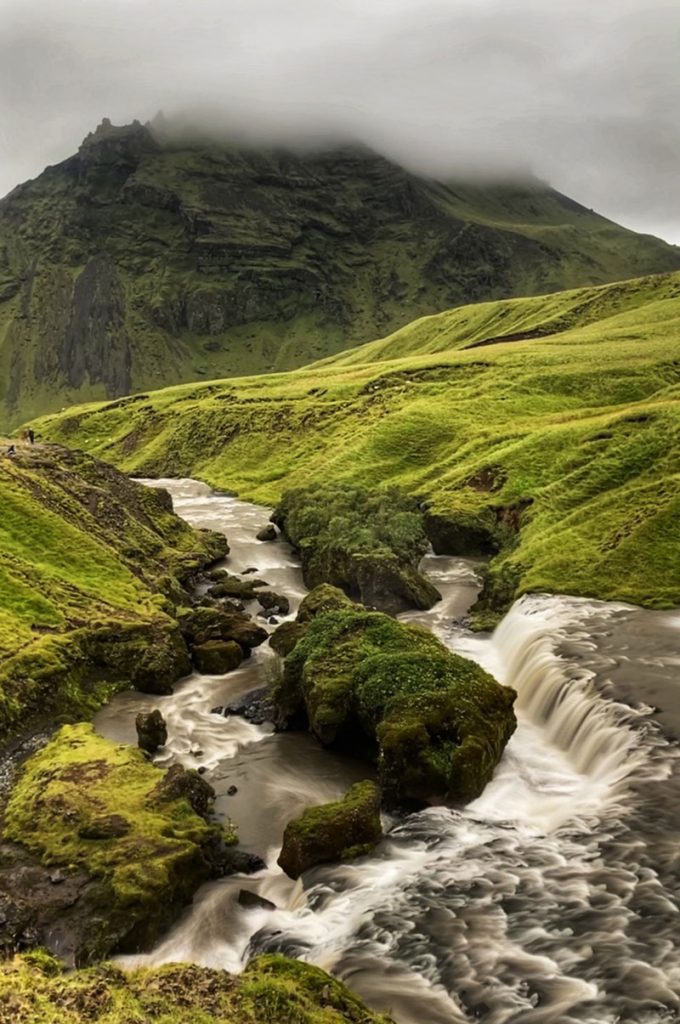 A raging stream cuts through green treeless hills