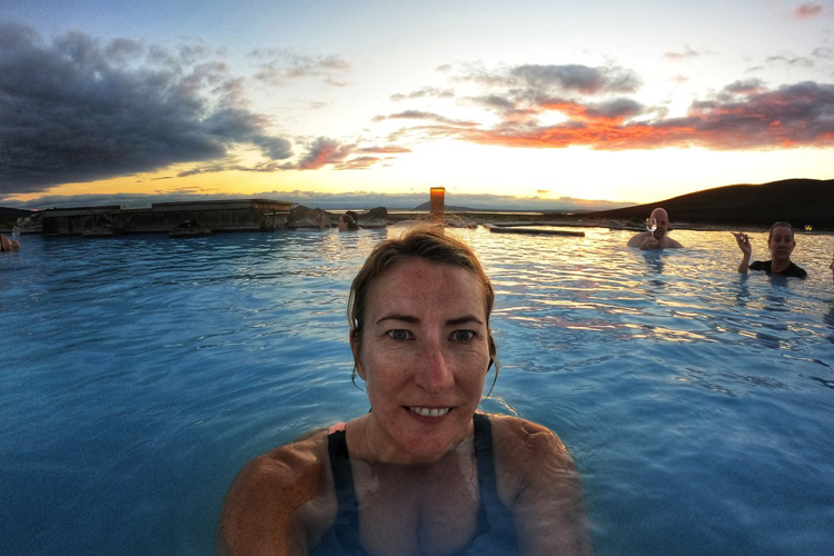 Woman sitting in a pool of water at dusk with an orange sunset behind