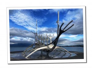 A large metal sculpture of a viking ship sits by a large lake