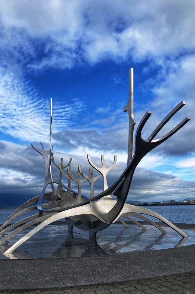 A large metal sculpture of a viking ship sitting by a large lake