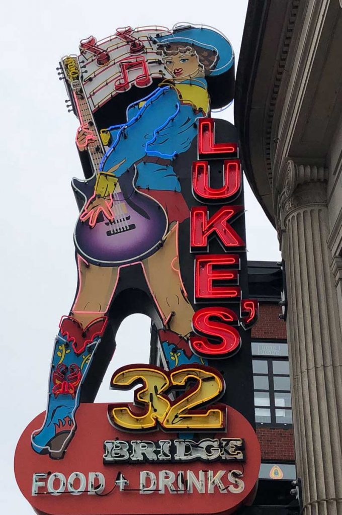 A large neon sign depicting a cowgirl with a purple guitar with the words Lukes 32 running down the length of the sign