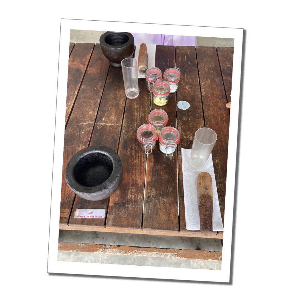 Assorted glass bottles of ingredients grey stone pestle and white glass bottle with plastic spoon and a note written on a table with the words Hot! Please don't touch on it