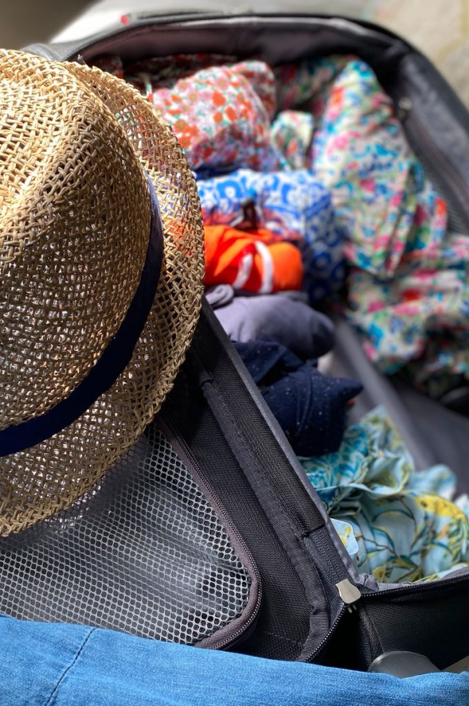 A Straw hat and out of focus clothes in a suitcase with red and white text overlay