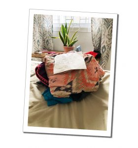 A packed open suit case on a bed with a hand written note on top on a bright bedroom setting
