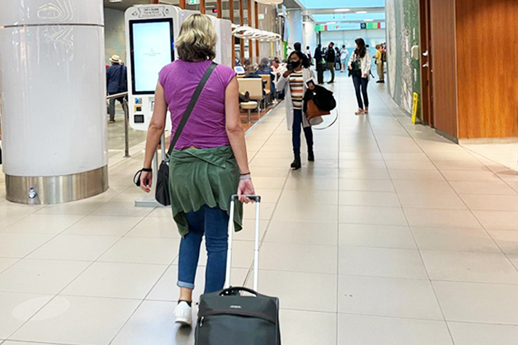A blonde Woman with a pink top wheeling a case away from the camera in an airport