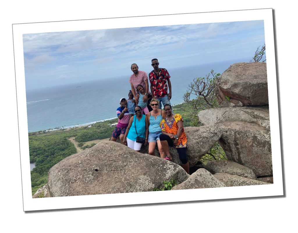 A group of people standing leaning on some large rocks overlooking the sea