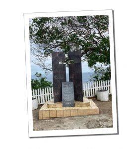 A cross shaped monument in a grave yard overlooking the sea