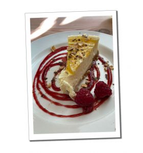 a slice of Cheesecake on a plate with raspberries and a circular pattern of sauce