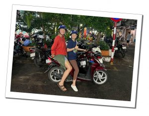 Two women on a stationary motorbike smiling for the camera