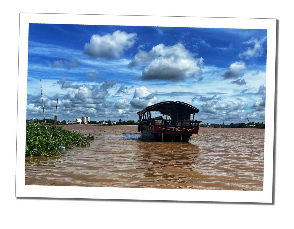 A Vietnamese boat floating on a brown river with a distant city setting