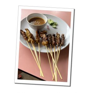 8 sticks of satay and a dip on a white plate