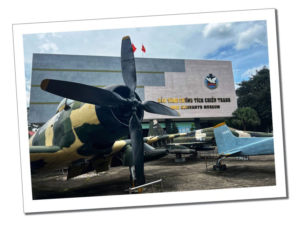 A large camouflaged propellered aeroplane standing in front of a rectangular front building