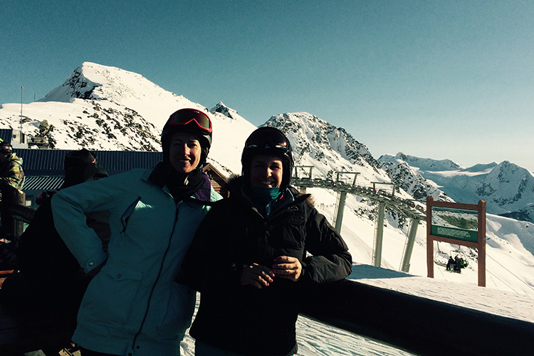Two women standing in snowy mountains at a ski resort overlooking the chairlift
