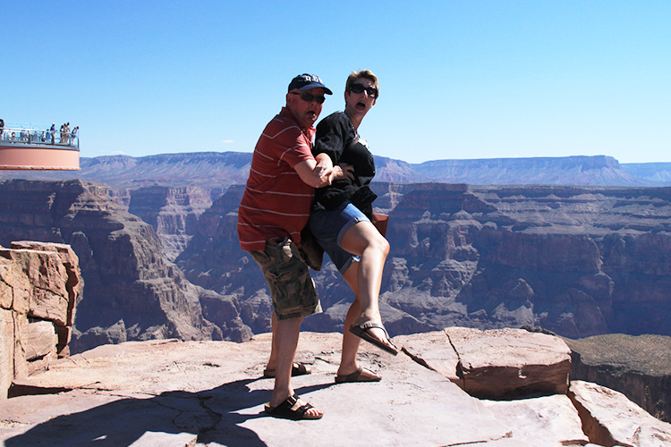 A man and a woman pretending to jump standing on a rock close to the edge of grand canyon