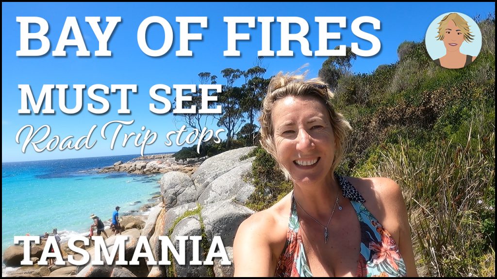 A blonde woman in a bikini top smiling on some rocks by a beach