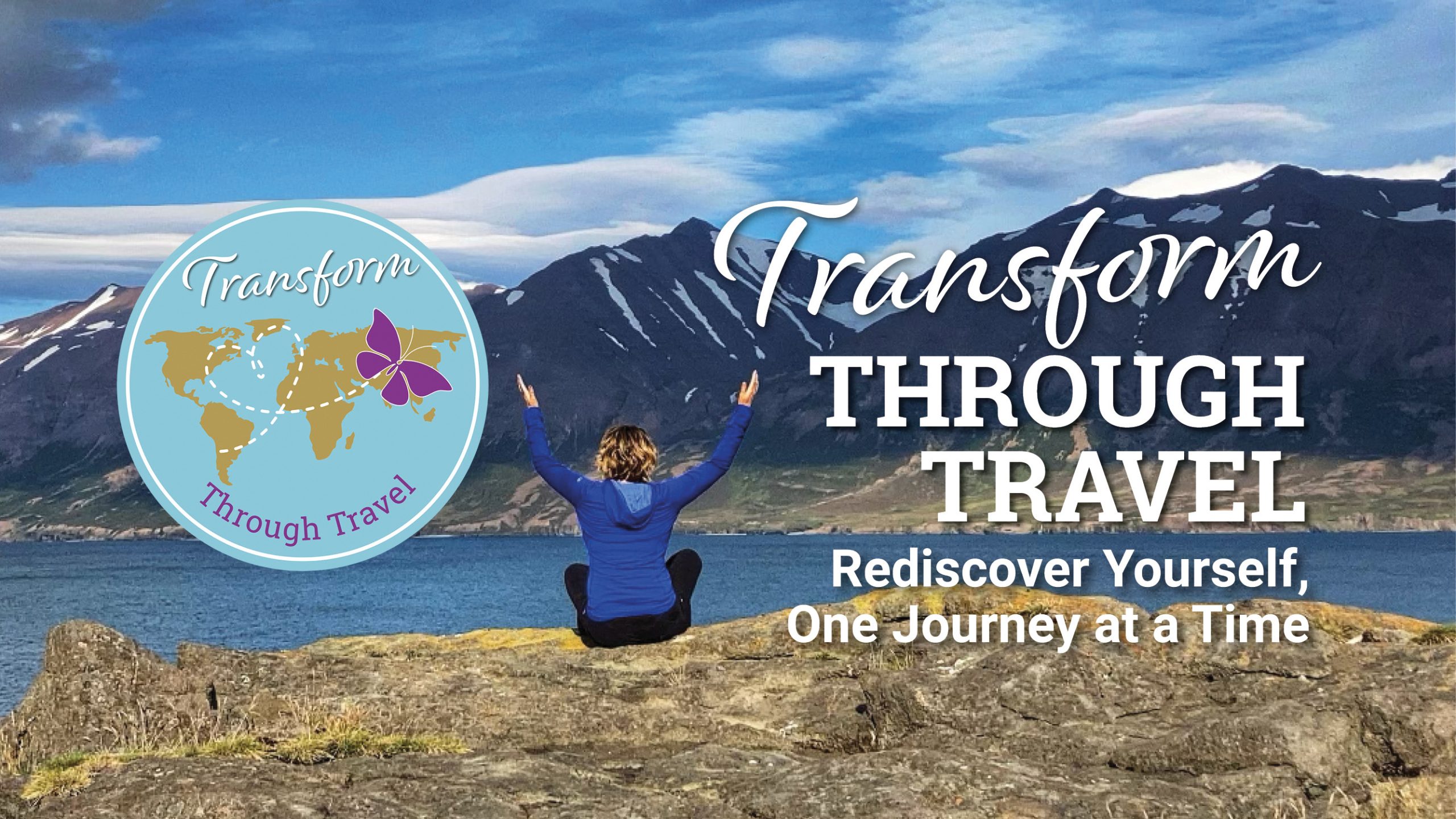 A person sitting on a rock with their arms outstretched overlooking a large stretch of water with a mountainous background