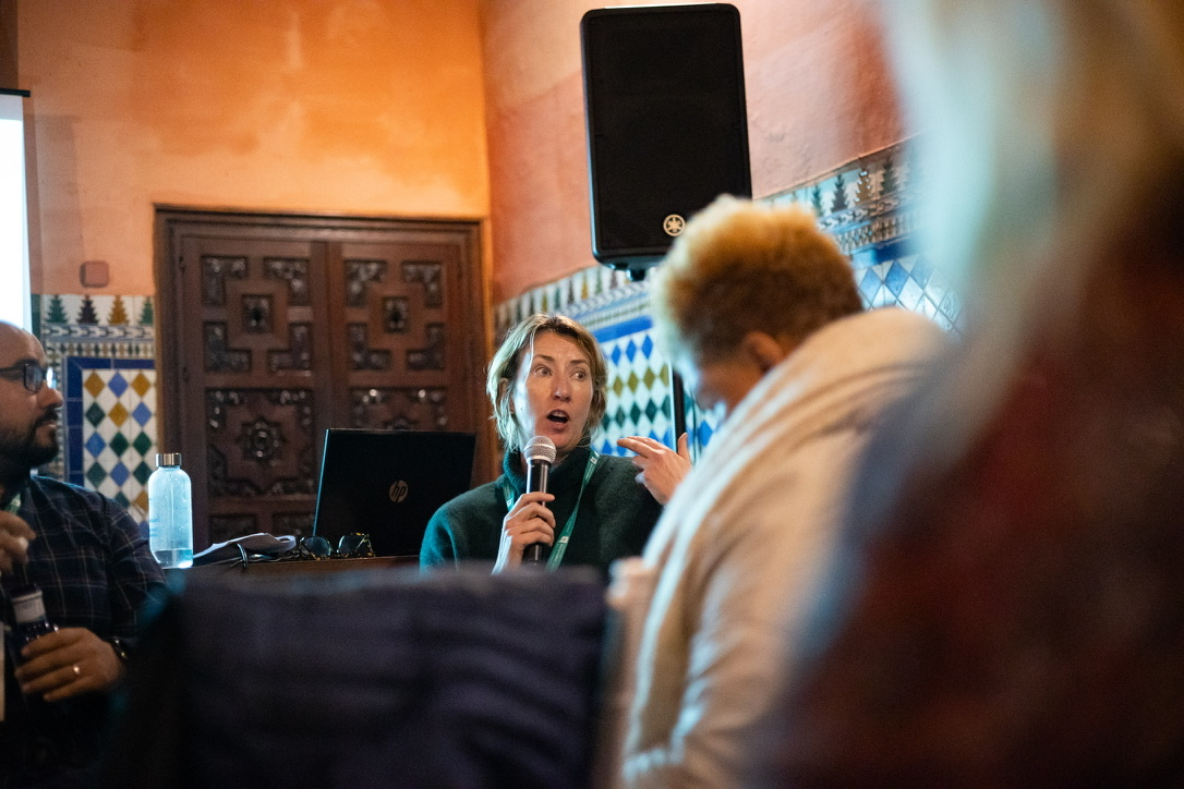 A blonde woman speaking on a microphone in a crowd