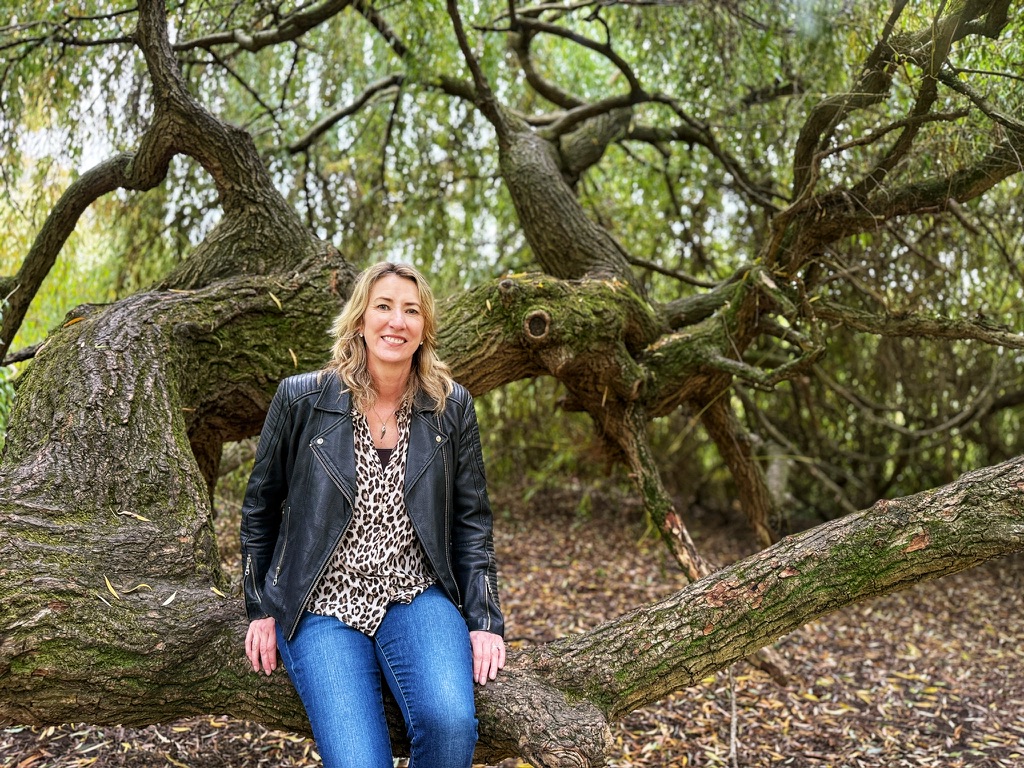 A blonde woman in jeans leaning up a tree
